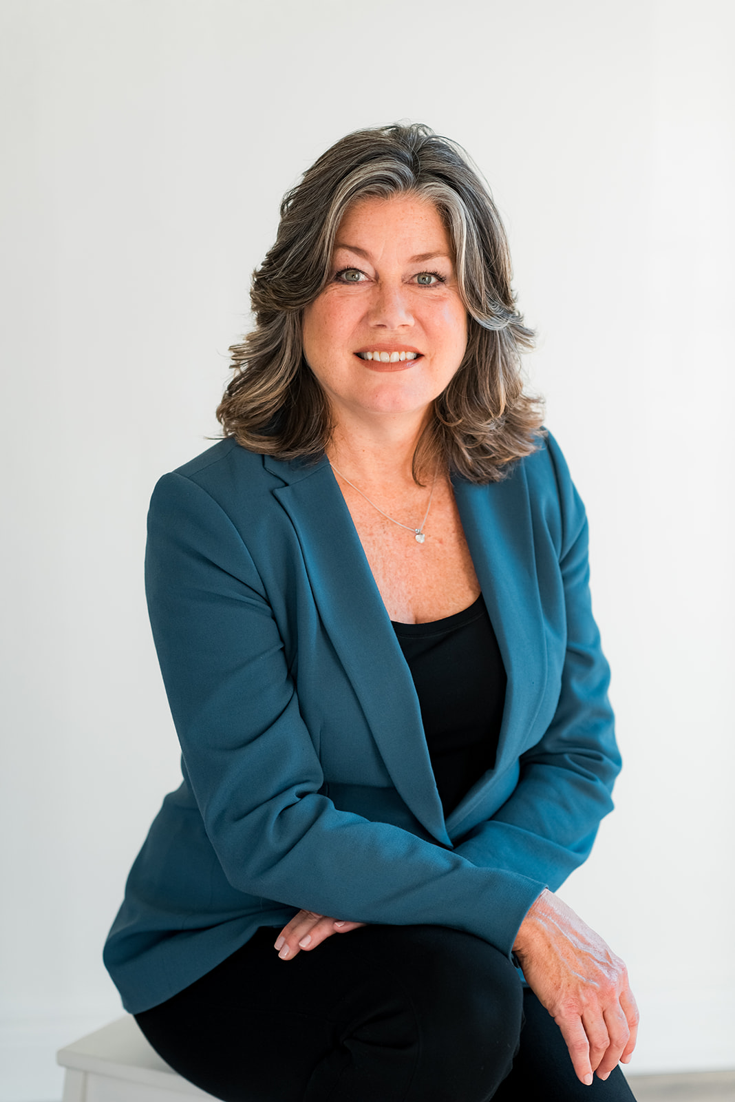 headshot of woman sitting down and smiling at camera with a grey background.